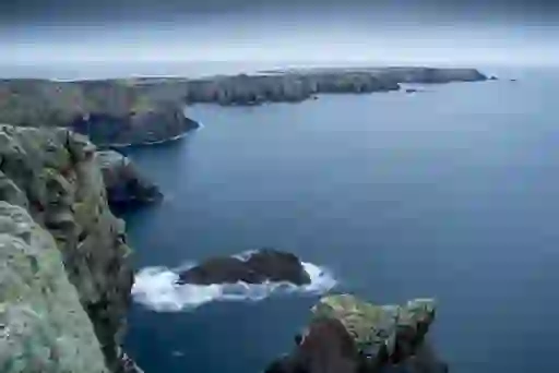 Tory Island cliffs extending into the Atlantic Ocean with jagged rocks rising above the surf.