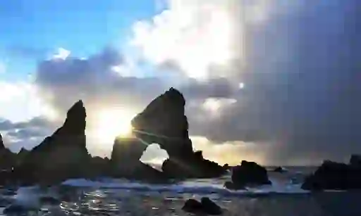 Walkers climbing grassy cliffs above sea arch and rock stacks on Donegal’s coast.