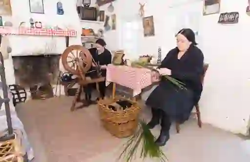Women weaving rushes and spinning wool beside the fireplace in cottage at Colmcille Heritage Centre.