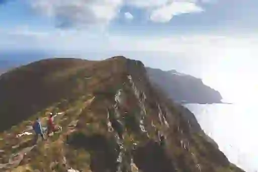 Hikers on ridge path overlooking sea cliffs at Slieve League in County Donegal.
