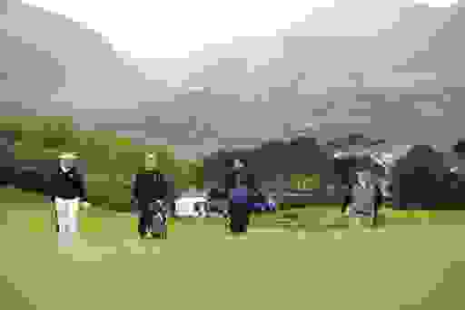 Golfers walking at Royal County Down, framed by the Mourne Mountains and town spire in the scenic backdrop.