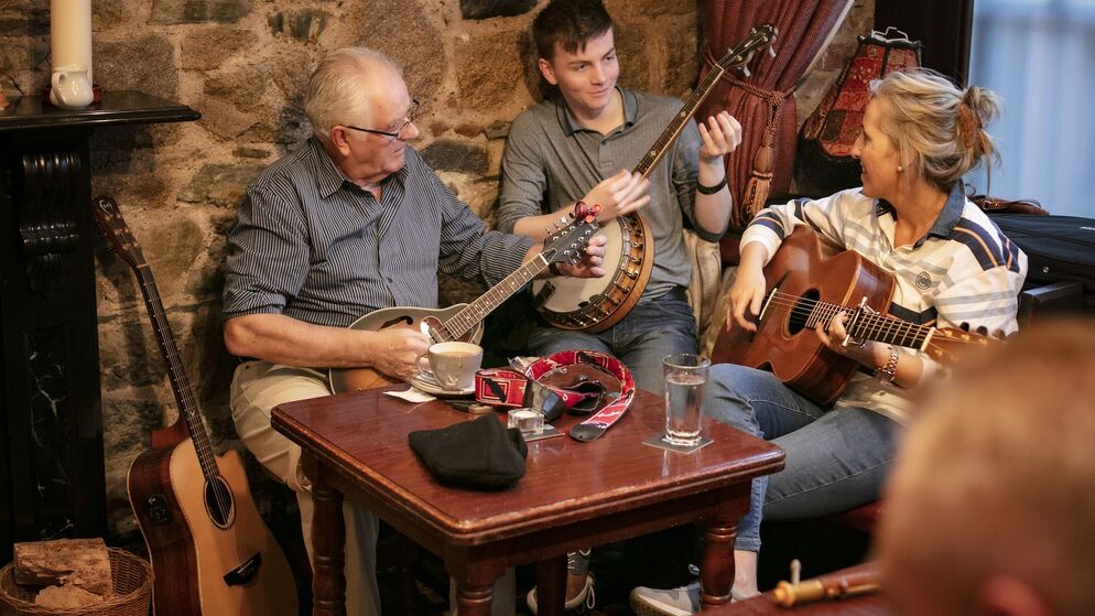Three musicians seated in a cosy pub playing mandolin, banjo and guitar during a traditional Irish music session.