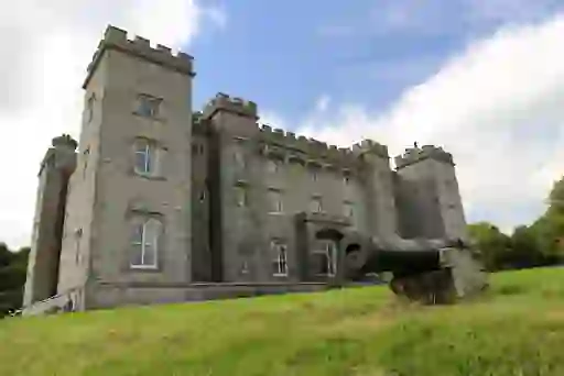 Stone façade of Slane Castle with a historic cannon in the foreground on a sloping lawn in County Meath.