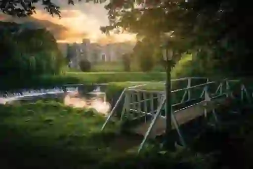 White footbridge over a stream with a view of Bellingham Castle and sunset glow in County Louth.