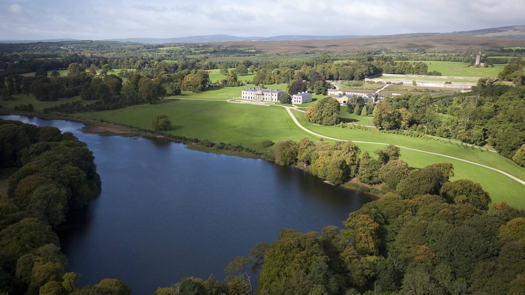 Aerial view of the grand Ballyfin Demesne with a lake and forest surroundings, offering luxury stays in the County Laois countryside.