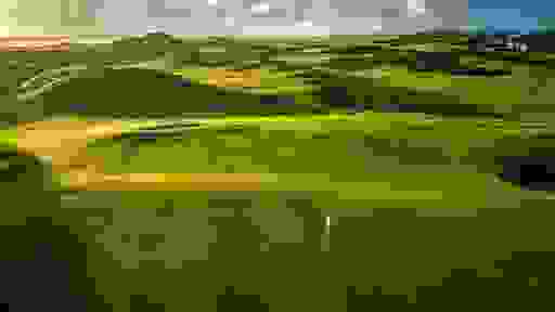Golden light sweeps across lush links fairways, shadows stretching over rolling dunes on a coastal golf course.