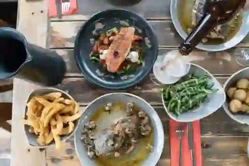 Overhead view of seafood dishes, chips, vegetables, and a drink being poured at a rustic wooden table.