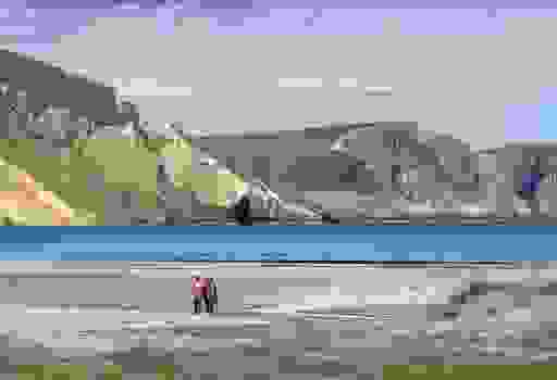 Couple walk along Keem Bay’s sandy beach, framed by soaring cliffs and calm blue Atlantic waters.