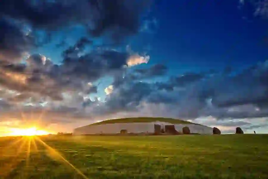 Winter sunrise casting golden light over Newgrange’s grass-covered mound and stone entrance.
