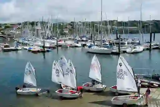 Children prepare small sailboats at Kinsale Harbour in County Cork, with dozens of yachts docked in the background.