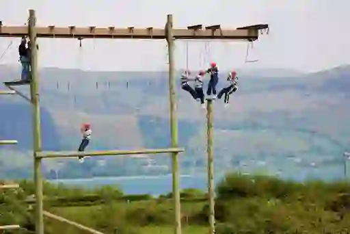 Teens in helmets balance on a high ropes challenge course overlooking Carlingford Lough and the Mourne Mountains.