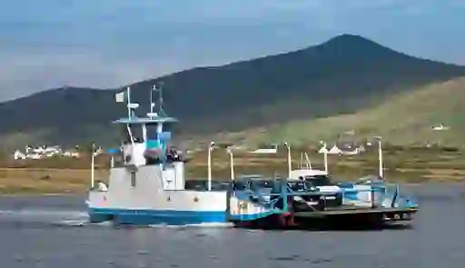 Car ferry transporting vehicles between Valentia Island and County Kerry, with green hills in view.