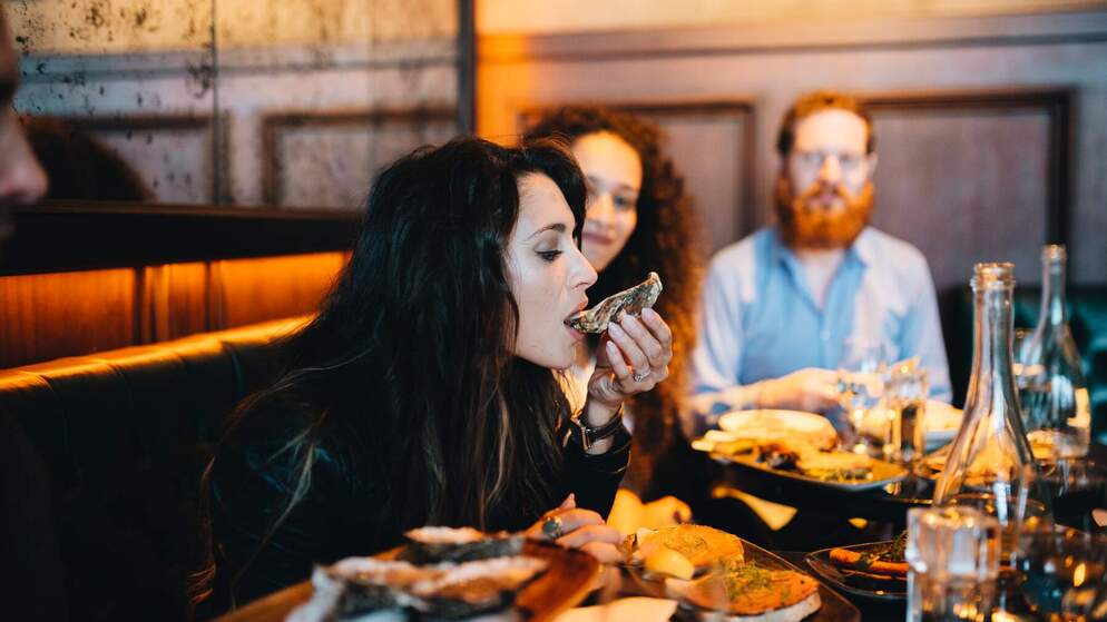 Woman eating an oyster at a restaurant with friends in Ireland.