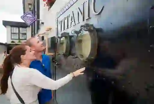 Smiling couple looking through portholes on a black Titanic-themed display at an attraction in Cobh.