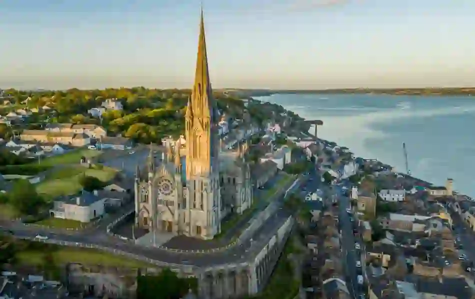 Aerial view of St Colman’s Cathedral and the coastal town of Cobh at sunset, overlooking Cork Harbour.