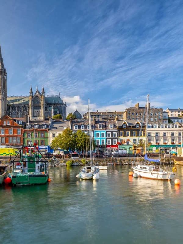 Colourful harbourfront buildings and St Colman’s Cathedral in Cobh, County Cork, viewed from the water on a sunny day.
