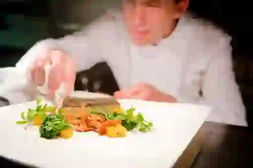 Chef adding final touches to a plated dish at Lough Erne Resort in Fermanagh, garnished with greens and chanterelle mushrooms.