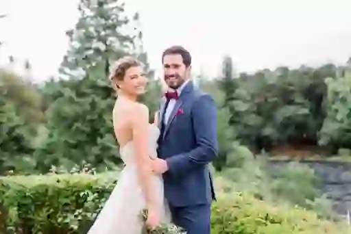 Bride and groom standing arm in arm at Ballynahinch Castle in County Galway, smiling in front of river and forested backdrop.