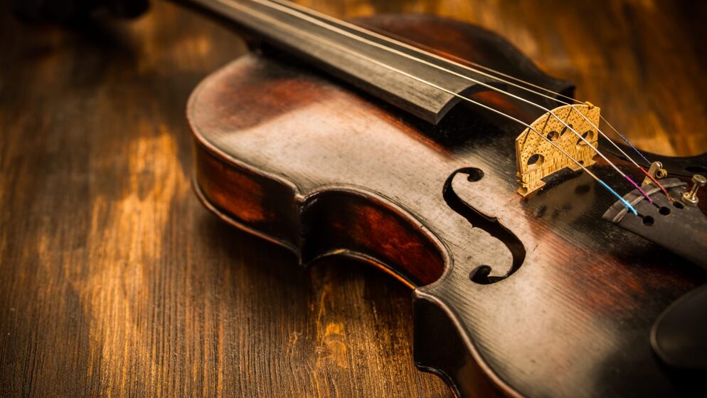Close-up of a worn Irish fiddle on a wooden table, its golden bridge and warm body lit softly to show fine craftsmanship.