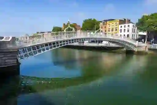 Morning view of Ha’penny Bridge over River Liffey, with Georgian buildings and reflections in calm water.