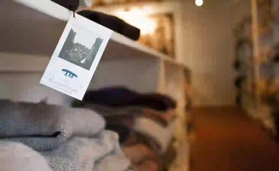 Close-up of an Inis Meáin knitwear tag hanging in a shop with folded Aran jumpers in the background.