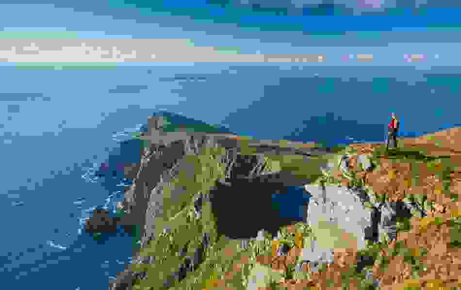 Walker standing atop a cliff on Achill Island, with panoramic views of Croaghaun cliffs, Keem Bay, and the Atlantic Ocean.