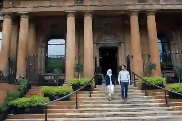 Couple walking down steps of Belfast’s Merchant Hotel, a grand historic building with columns.