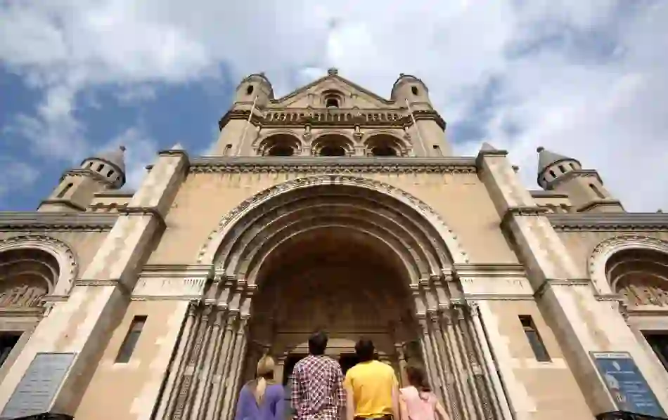 Four people admire the grand stone entrance and Romanesque arches of St Anne's Cathedral on a cloudy day.