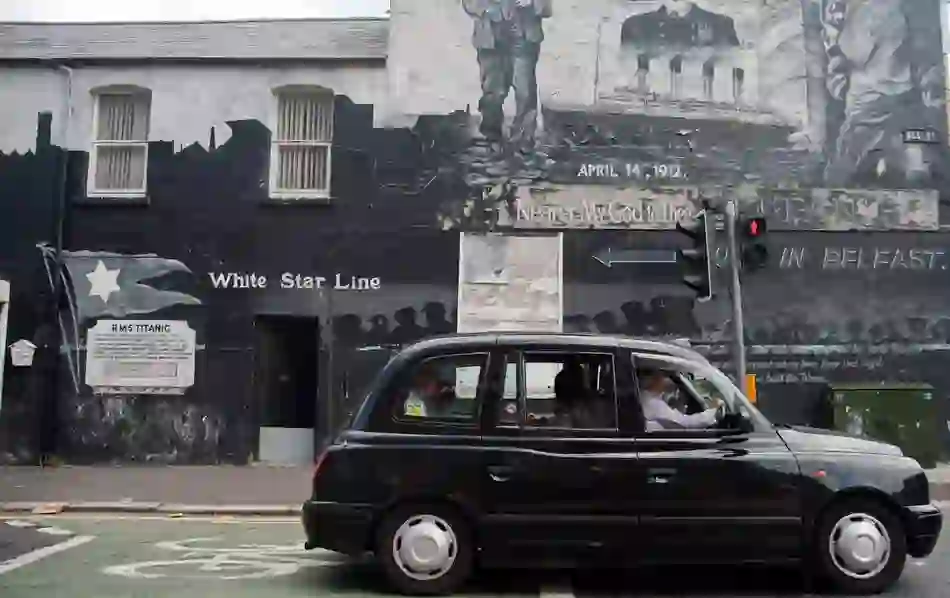 Black taxi drives past a Titanic mural on a gable wall in East Belfast commemorating the 1912 tragedy.