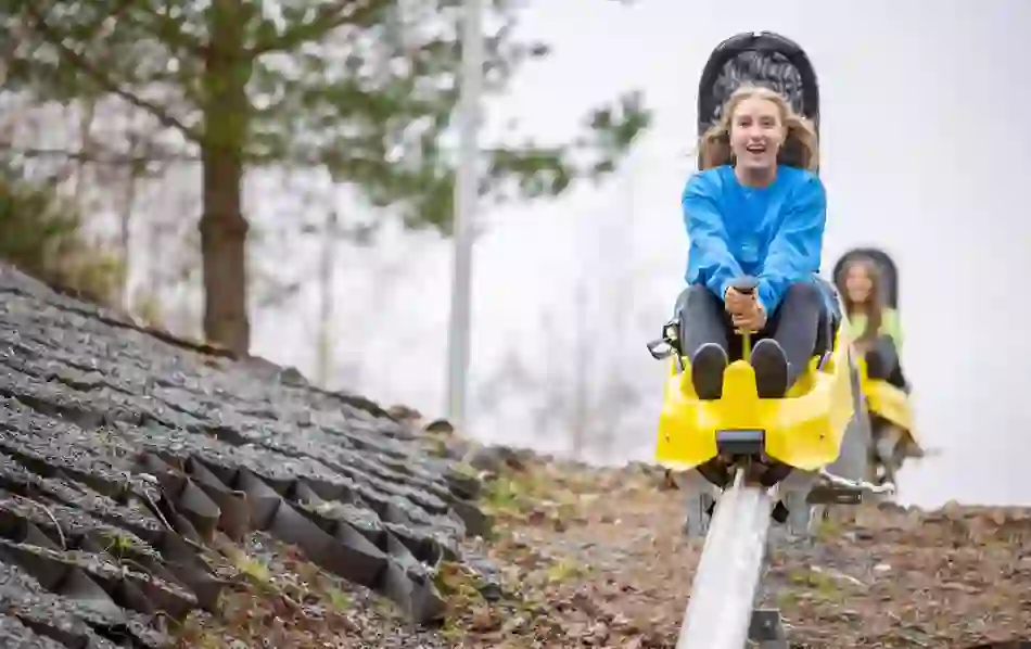 Young woman riding the zipline roller coaster at Colin Glen Forest Park, smiling.