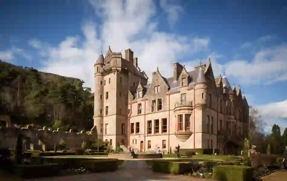 Belfast Castle with visitors walking in its formal gardens, set against Cave Hill.