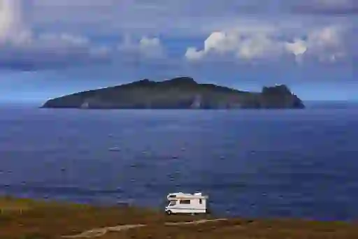 A motorhome parked on a clifftop in Dingle, Kerry, facing the Atlantic Ocean with views of a dramatic island offshore.
