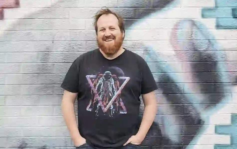 Adam Turkington, Street Art Walking Tour guide, smiling against a colourful graffiti wall in Belfast.
