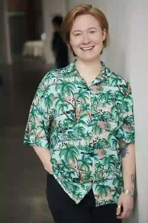 Rae Watterson smiling inside The MAC, Belfast, wearing a patterned shirt with palm trees.