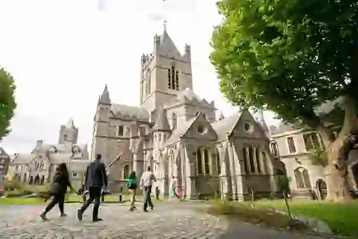 Visitors walking through the grounds of Christ Church Cathedral, Dublin, under leafy trees.