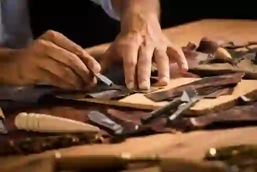 Hands crafting leather pieces with precision tools on a wooden workbench.
