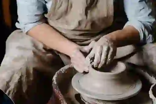 A potter shaping clay on a spinning wheel in a traditional pottery workshop.