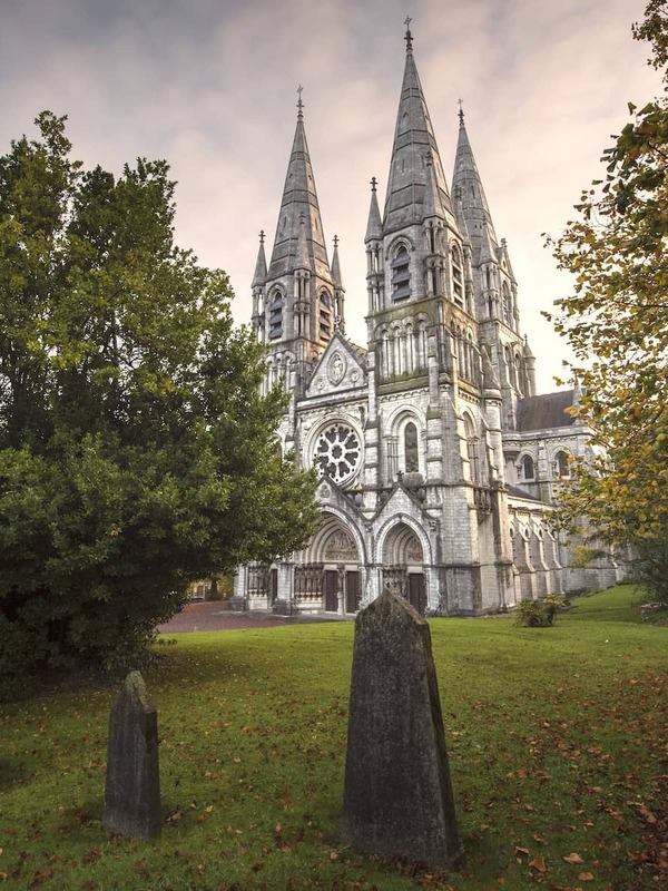 St Fin Barre’s Cathedral in Cork City, gothic spires rising above autumn trees and historic graveyard.
