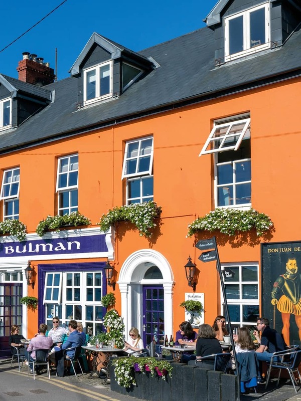 The Bulman pub exterior in Kinsale, County Cork, with bright orange façade and outdoor dining on sunny street.