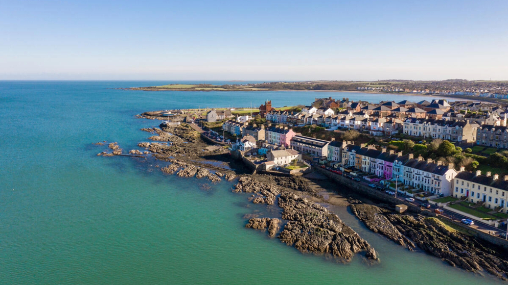Coastal view of Bangor with colourful seafront houses, rocky shoreline and calm blue sea under clear sky.