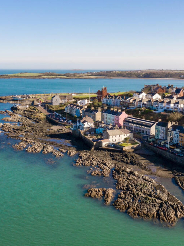 Coastal view of Bangor with colourful seafront houses, rocky shoreline and calm blue sea under clear sky.