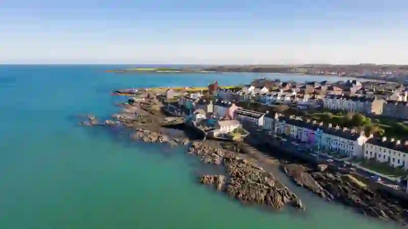 Coastal view of Bangor with colourful seafront houses, rocky shoreline and calm blue sea under clear sky.