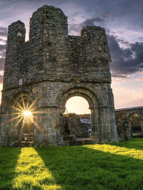 Mellifont Abbey ruins in County Louth at sunset with ancient stone arches, dramatic skies and long shadows across the grass.