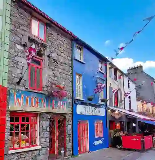 Colourful shopfronts on Quay Street, Galway city with bunting, cafés and traditional stone buildings.