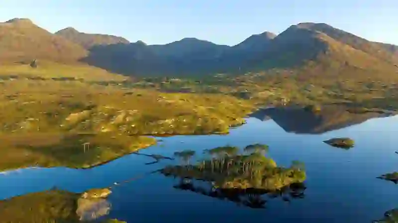 Derryclare Lough in Connemara, County Galway, with small wooded island, mountains and reflections in calm water.