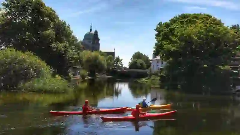 Kayakers on the River Corrib in Galway with cathedral, bridge and trees reflected in calm water.