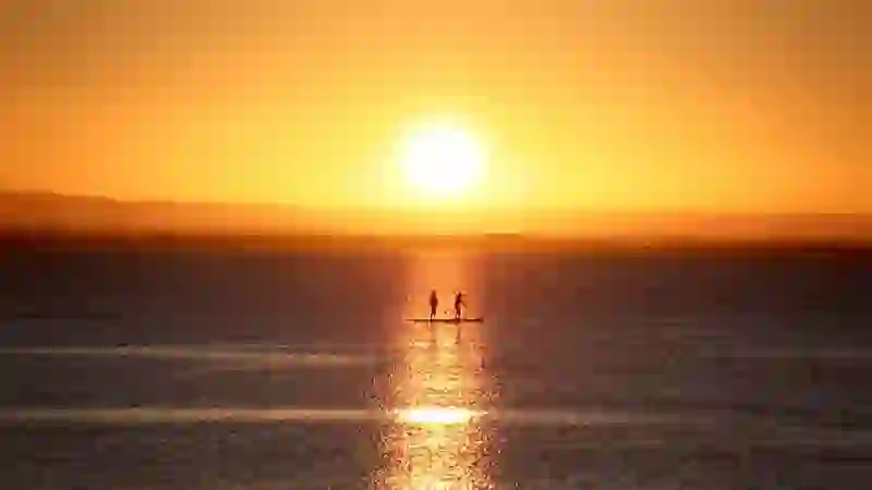 Silhouetted paddleboarders on Galway Bay at sunset with golden light reflecting across the sea.