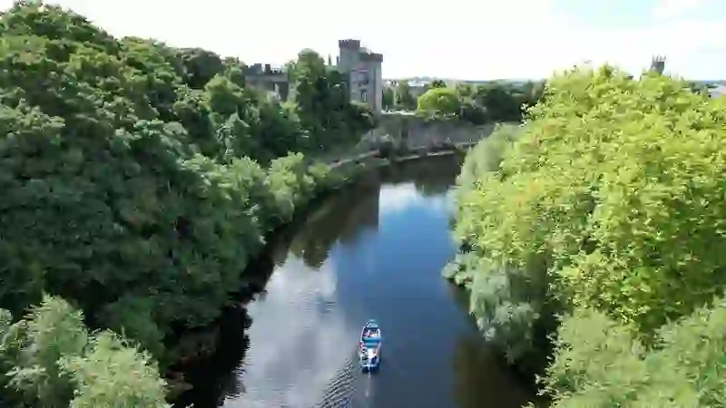 Boat trip on the River Nore with Kilkenny Castle and leafy banks in view.