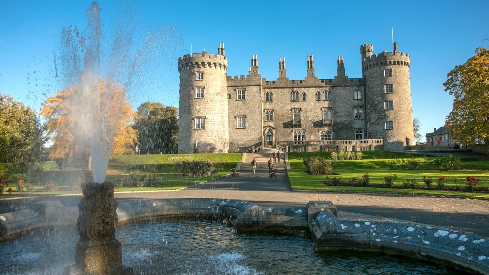 Kilkenny Castle reflected in a fountain, with manicured gardens and historic stone towers in Kilkenny city.