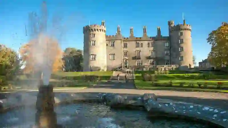 Kilkenny Castle reflected in a fountain, with manicured gardens and historic stone towers in Kilkenny city.